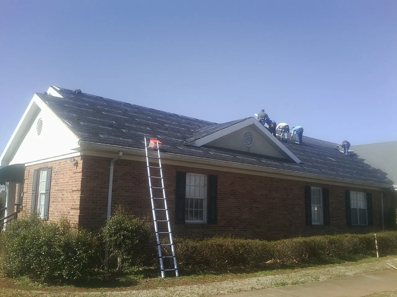 Crew tearing shingles off a brick ranch roof with a ladder set — Emergency Roof Repair work by our crew in Waterboro