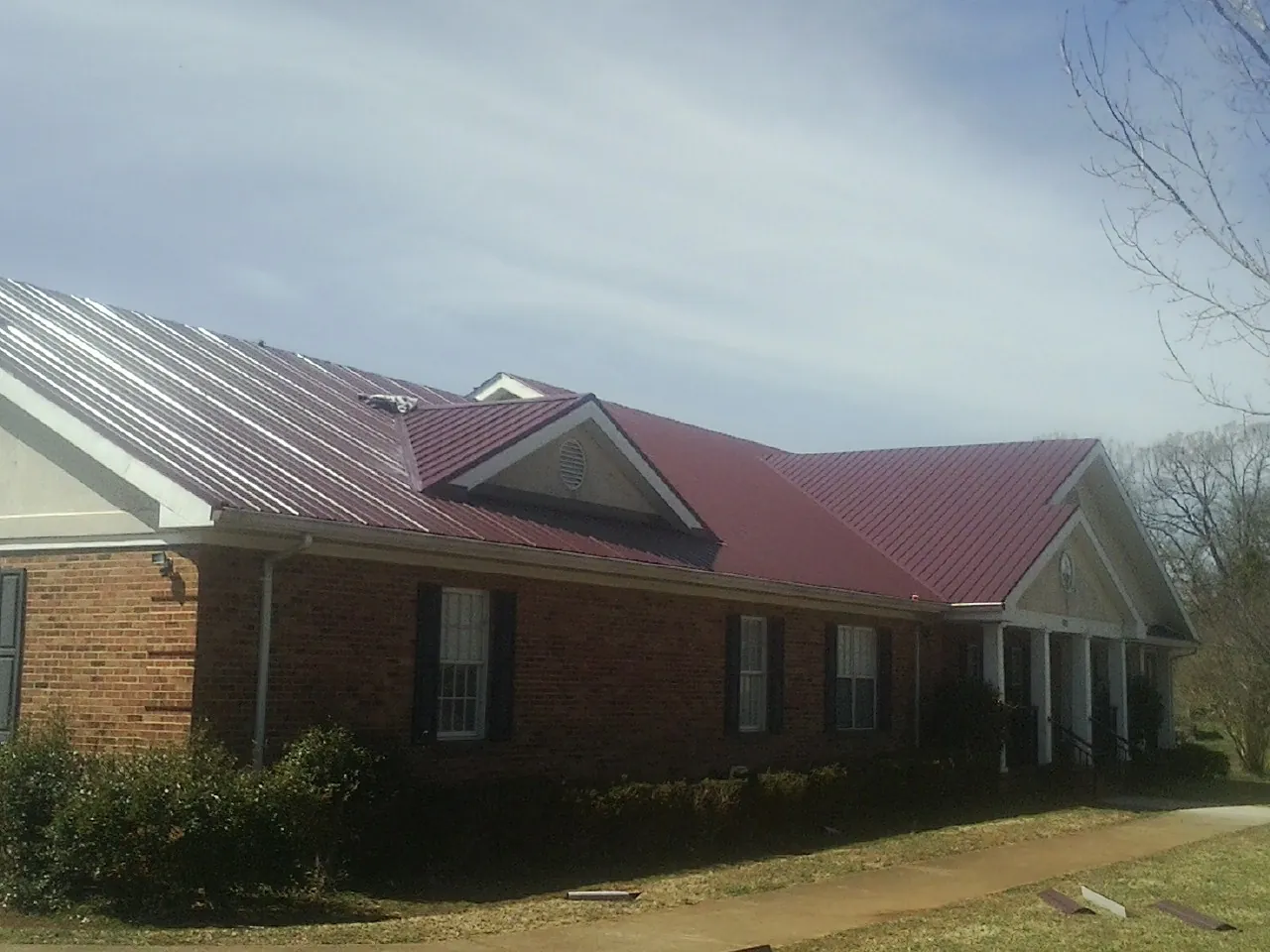 Red metal roof with gabled entries on a long brick building, from a Hail Damage Roof Repair job in Waterboro