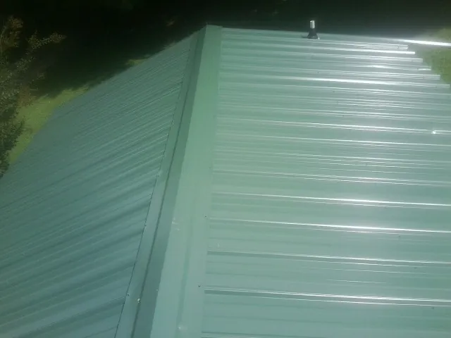 New green metal panels meeting at the ridge of a roof — Flat Roof Repair work by our crew in Waterboro