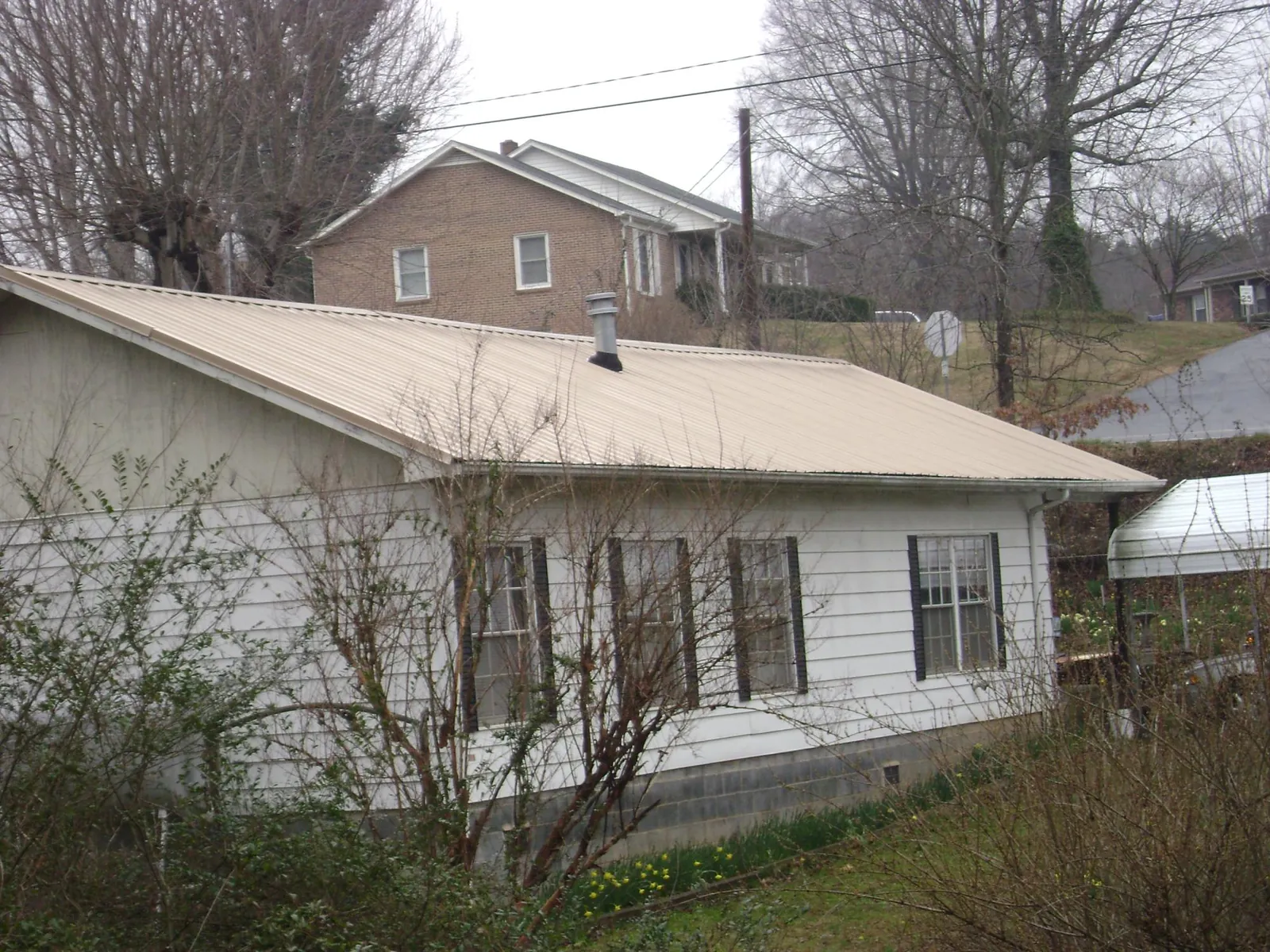 Tan metal roof on a white sided house set into a hillside — Commercial Roofing by Roofing Brothers in Waterboro