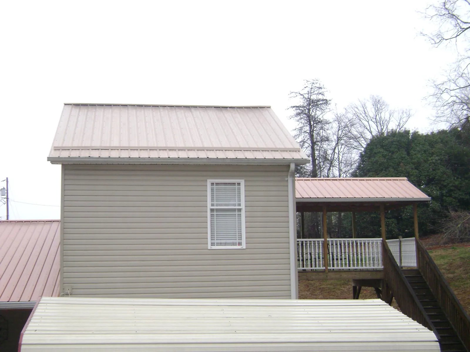 Tan metal roofs on a two story addition and attached porch, from a Roof Replacement job in Waterboro